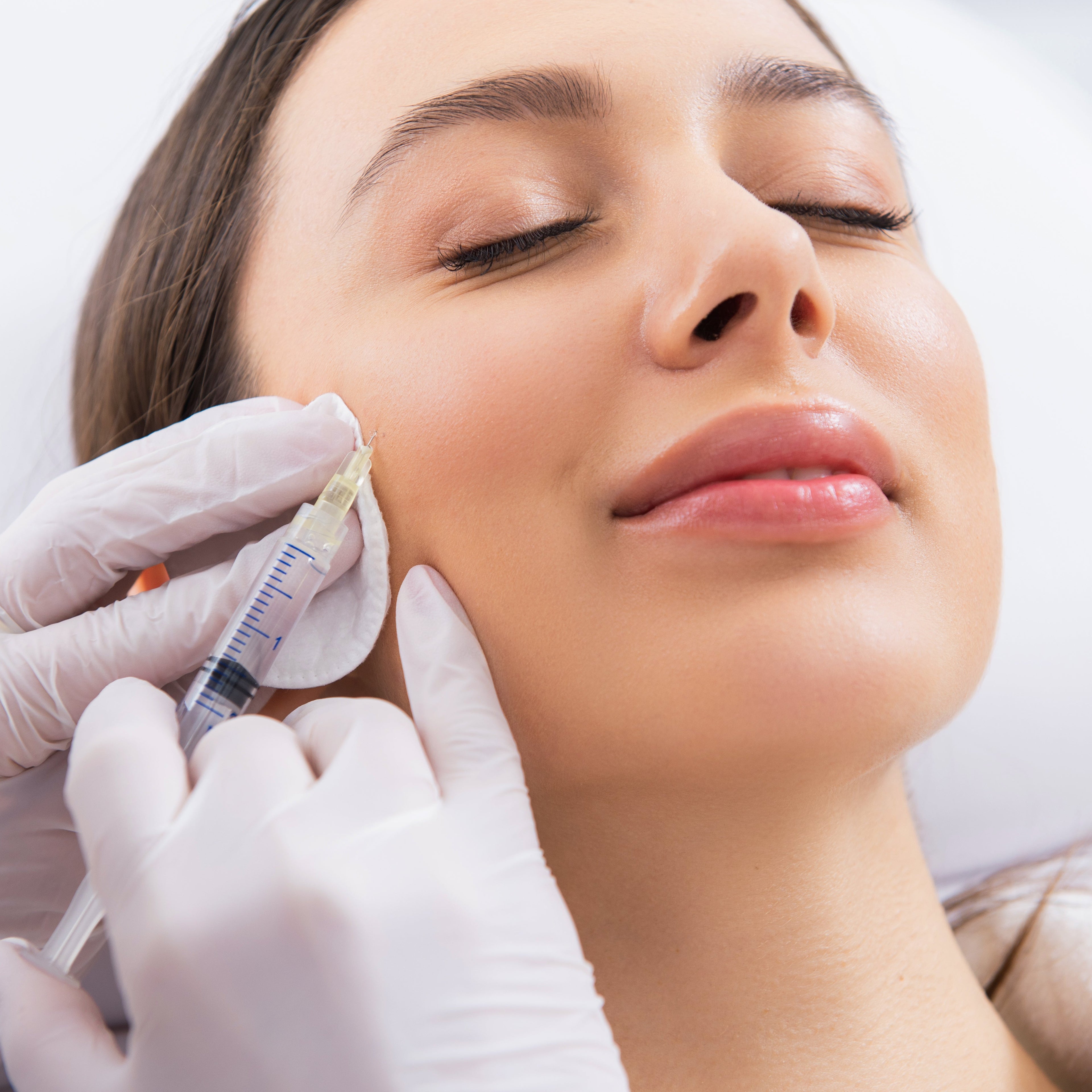 Woman receiving facial injection treatment with gloved hands holding a syringe.